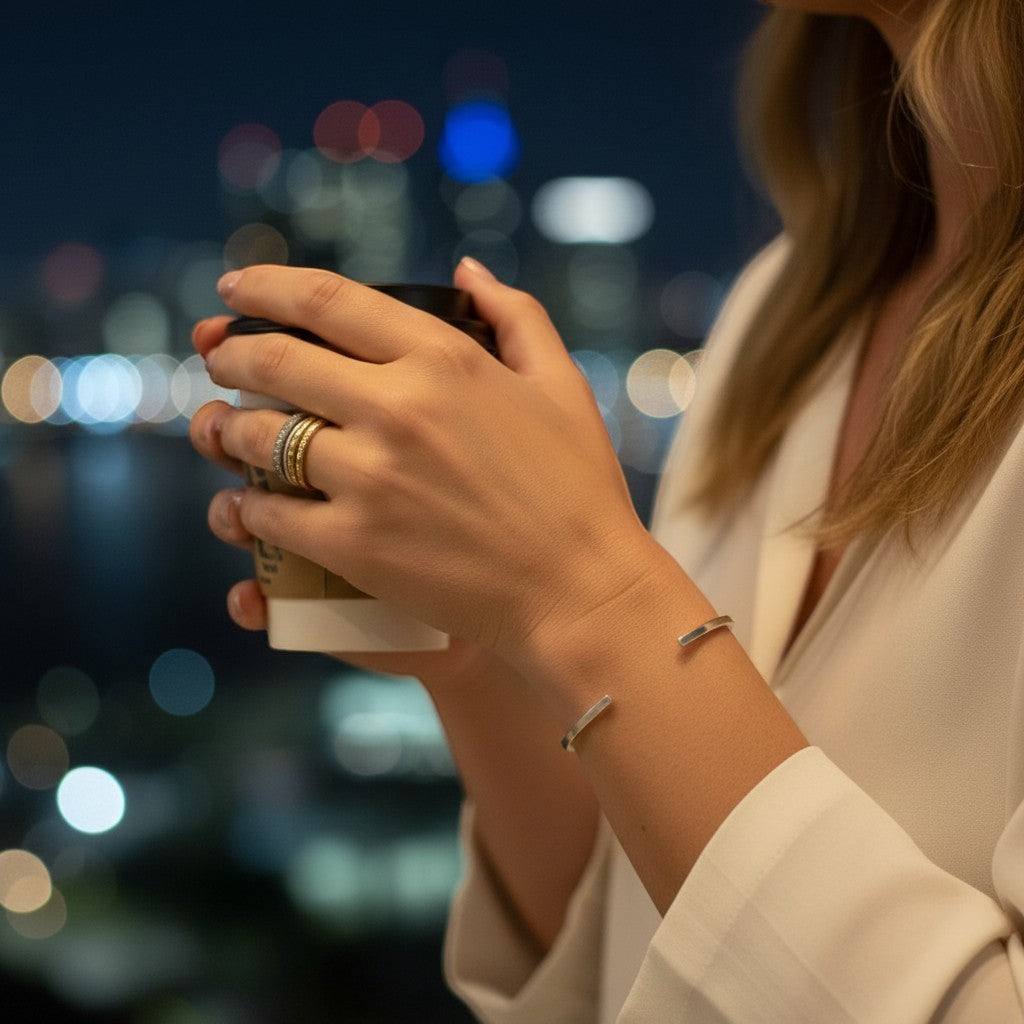 Pulsera esclava lisa de plata de Sophia Schneider Joyas en la muñeca de una mujer con fondo urbano nocturno